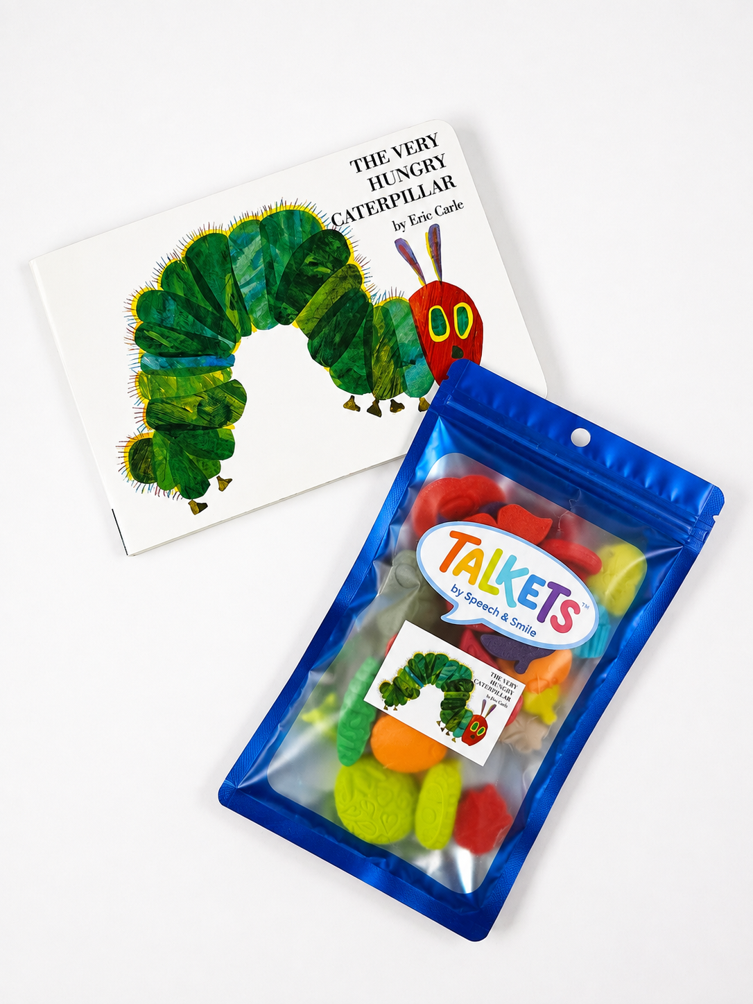 A children's gift set featuring the book 'The Very Hungry Caterpillar' by Eric Carle and a blue resealable pouch of colorful 'Talkets' speech-bubble toys. The book shows the classic green caterpillar illustration, and the pouch contains various colorful plastic speech-bubble toys visible through a clear window.