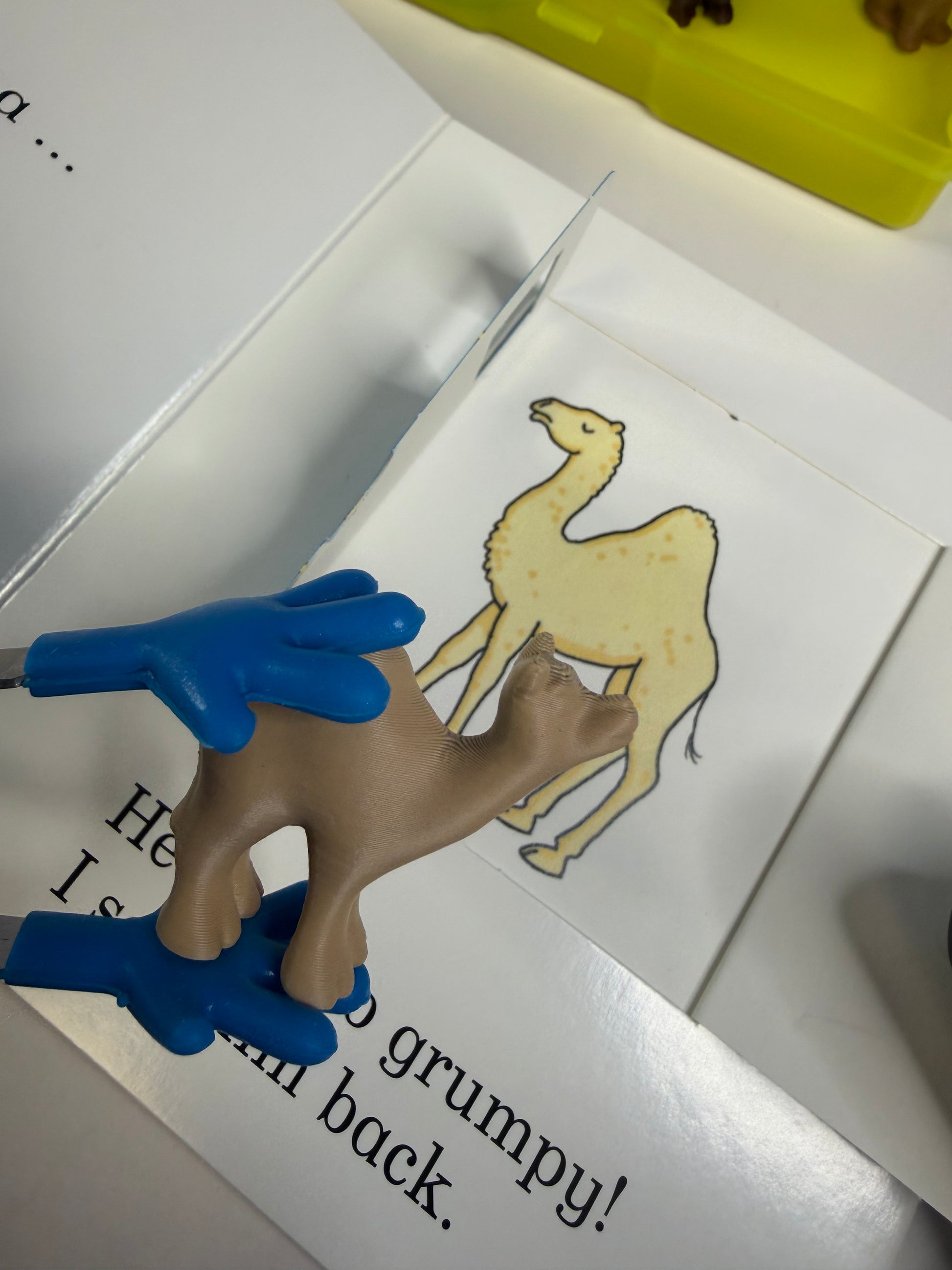 Toy figure of a camel with blue hands on top of a book with illustrations