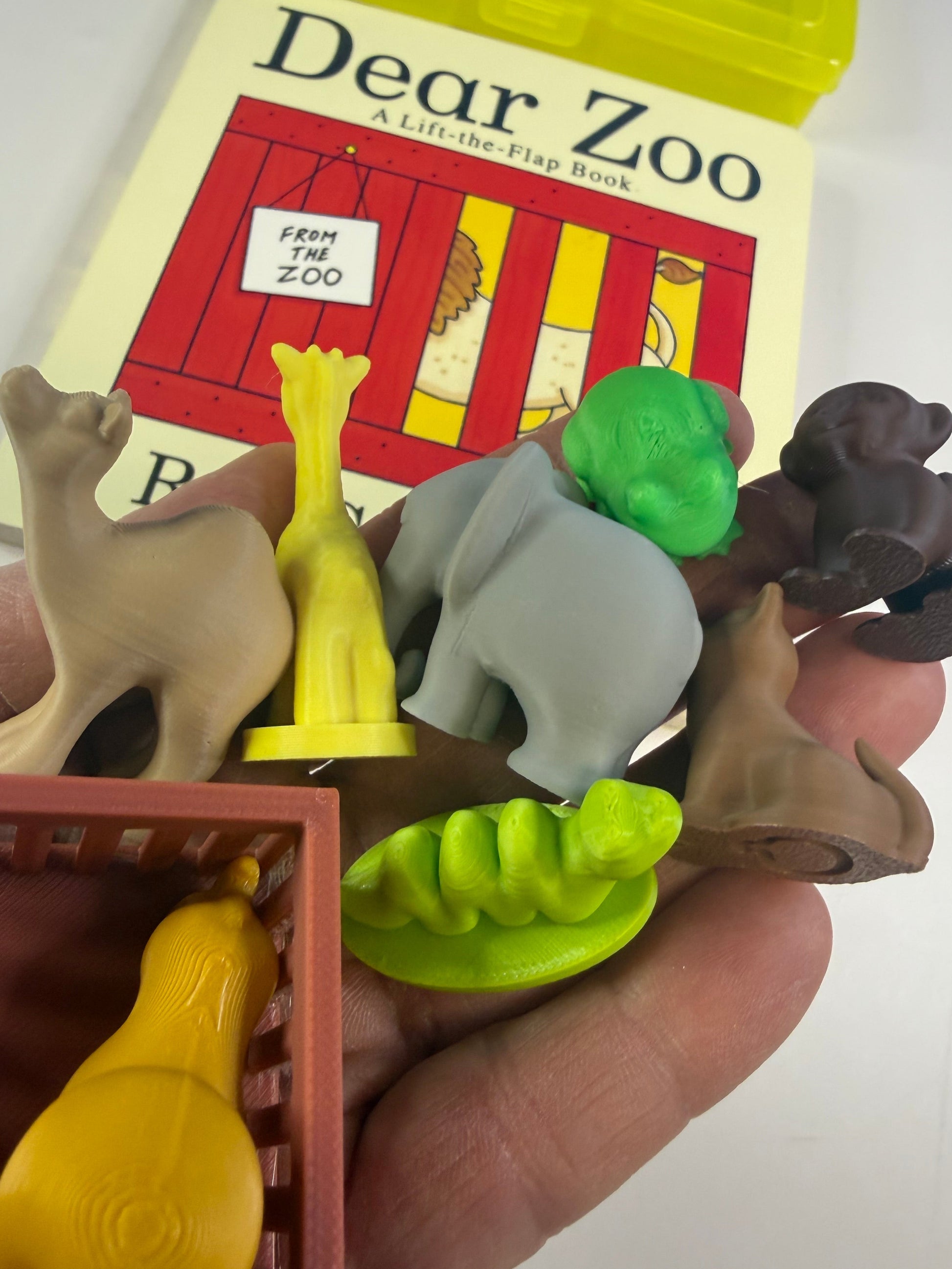 Toy animal figures held by a hand with a 'Dear Zoo' book in the background