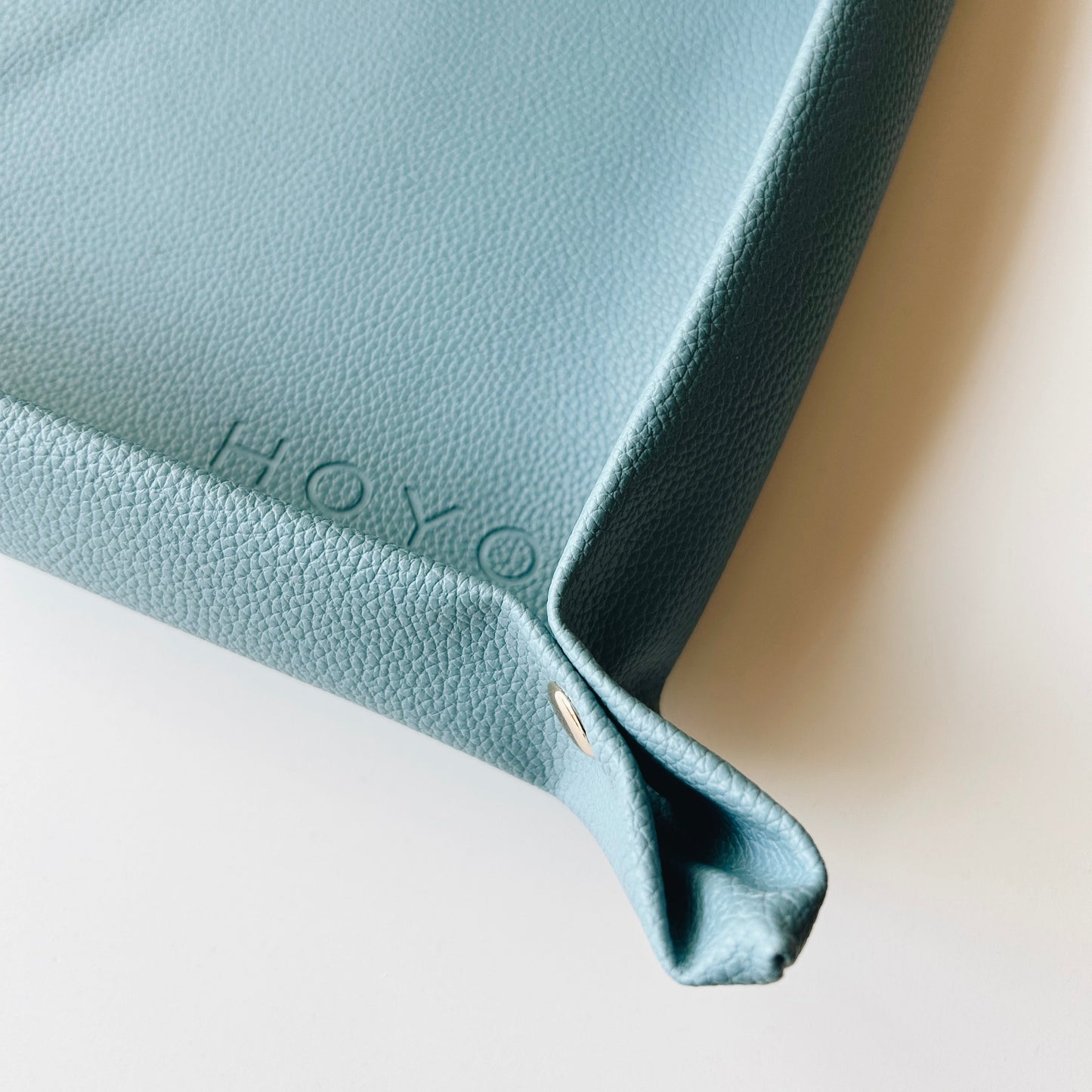 Close-up of a light blue leather product with 'HOYO' branding on a neutral background